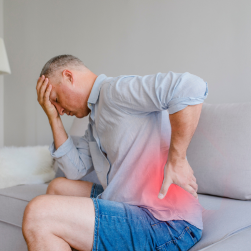 Man sitting down bent forward in discomfort holding lower back in pain. Lower back has a red glow showing pain area.