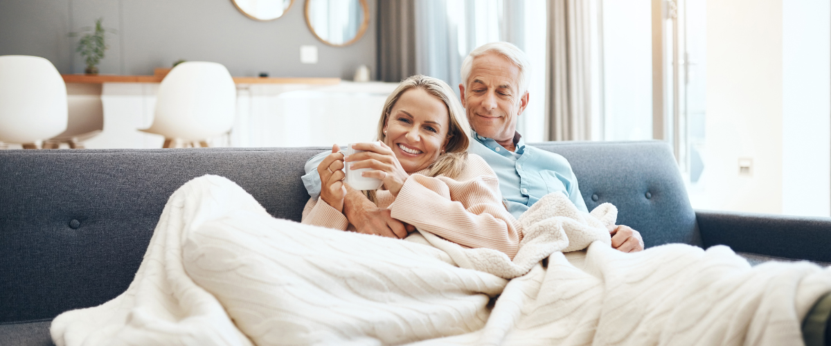 Man and woman happy and smiling sitting on navy sofa with white blanket around them