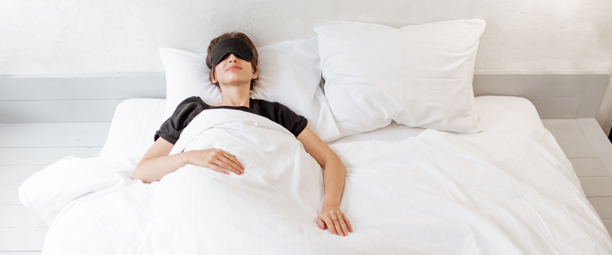 Woman with black top and sleep mask lying asleep on a white bed